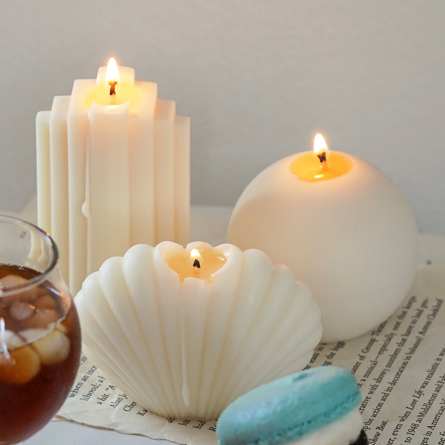 lit ribbed stair soy pillar candle, round sphere candle, and seashell shape candle on book pages