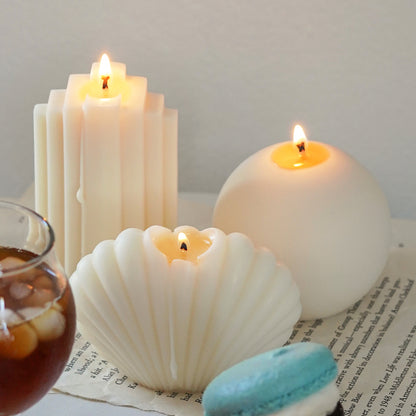 lit ribbed stair soy pillar candle, round sphere candle, and seashell shape candle on book pages