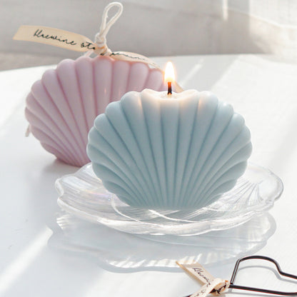 a lit aqua blue color seashell soy pillar candle on a holographic shell tray and lavender shell candle