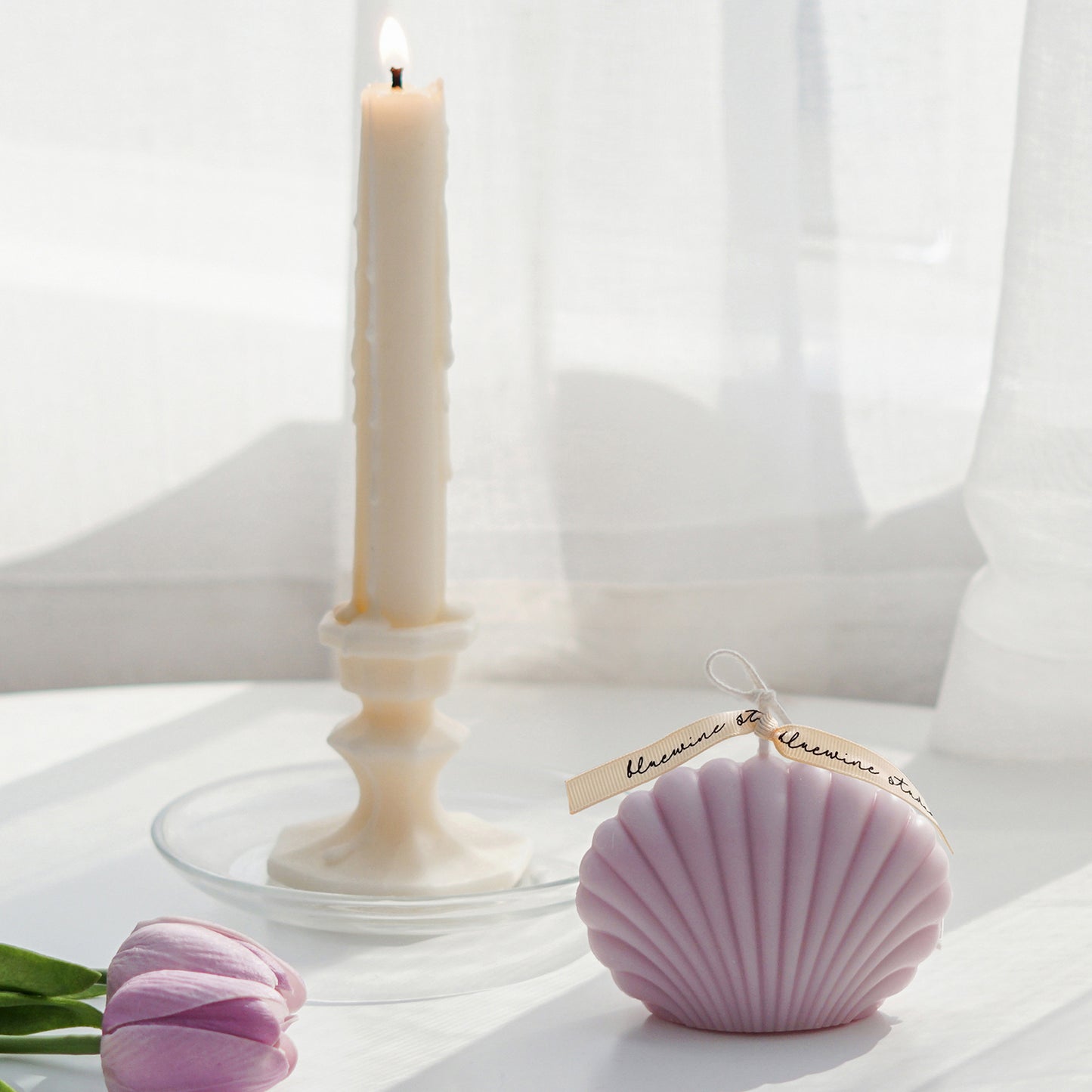 lavender seahsell soy pillar candle, lavender tulips, and a lit taper candle on a clear dish