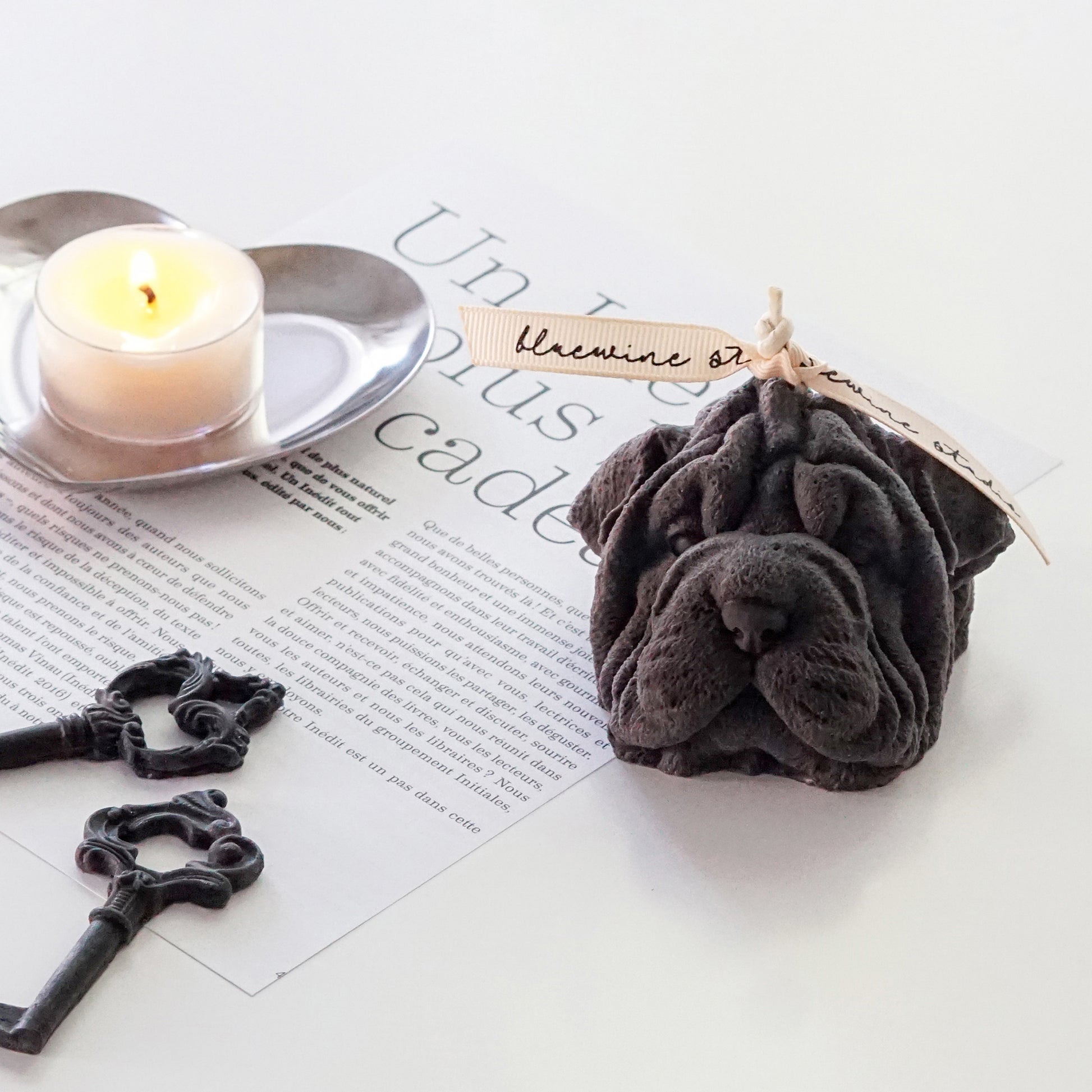 dark gray shar pei shape dog soy pillar candle with bluewine studio ribbon, black key shape wax melts, a lit tealight candle on a silver heart shape tray