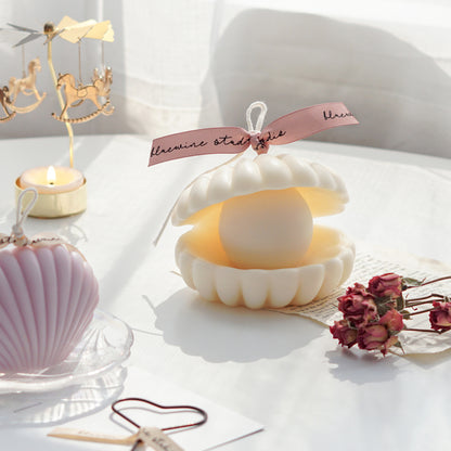 shell pearl white soy pillar candle with pink bluewine studio ribbon and pink dried roses, lavender seashell soy pillar candle on a holographic shell tray, and a lit tealight candle in a gold merry-go-round candle holder