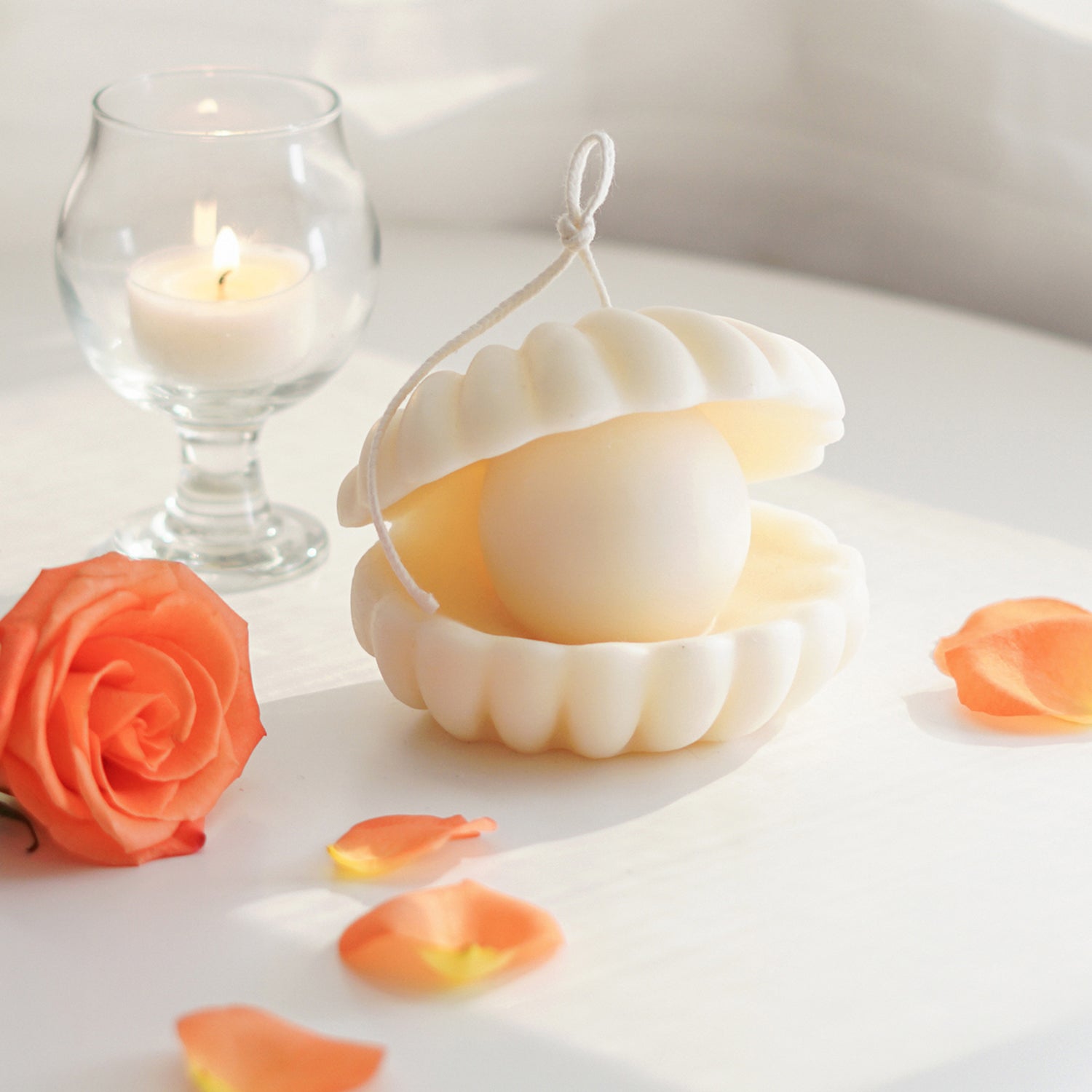 shell pearl shape soy pillar candle with long wick, orange rose and rose petals, and a lit tealight candle in a mini glass