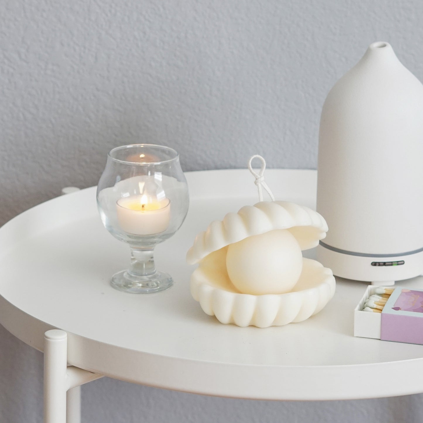 shell pearl soy pillar candle, a lit tealight candle in a mini glass, mint color matches, and diffuser on white round side table