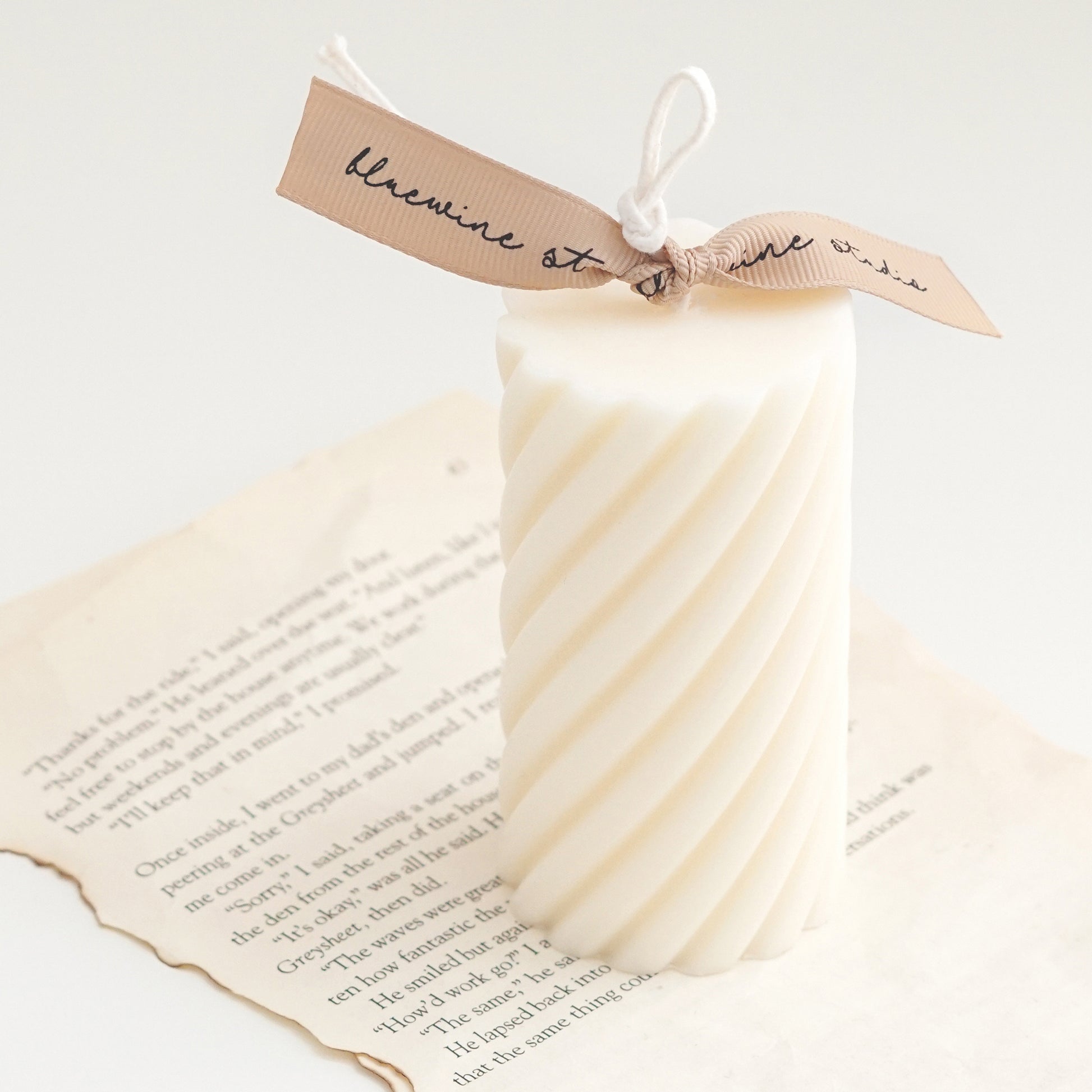 a white spiral cylinter soy pillar candle with beige bluewine studio ribbon on book pages