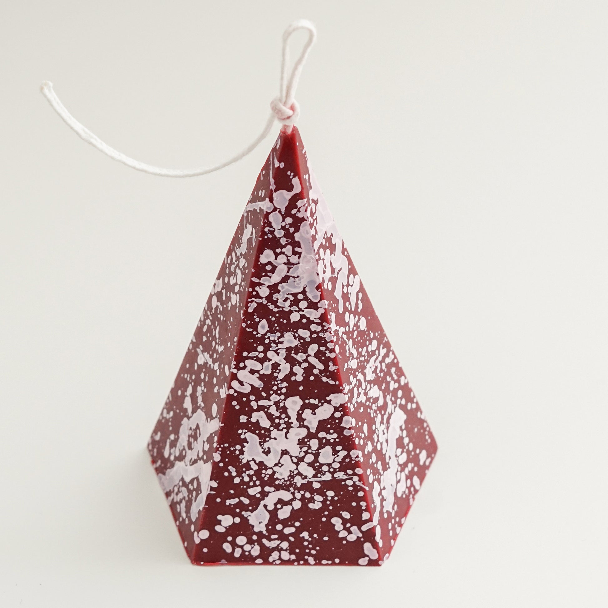 a burgundy color pentagonal pyramid shape soy pillar candle with white splatter pattern