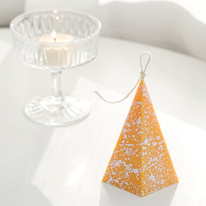a yellow pentagonal pyramid shape soy pillar candle with white splatter pattern