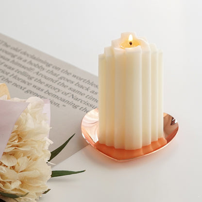 a lit stair shape sculptural white soy pillar candle on a heart shape rose gold tray and dried flower bouquet