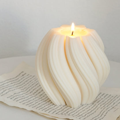 a lit swirl sculptural white soy pillar candle on book pages