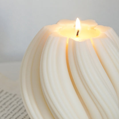a lit swirl sculptural white soy pillar candle on book pages