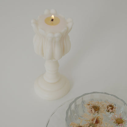 a tulip shape candle burning with a cup of tea with flowers in a glass tea cup set