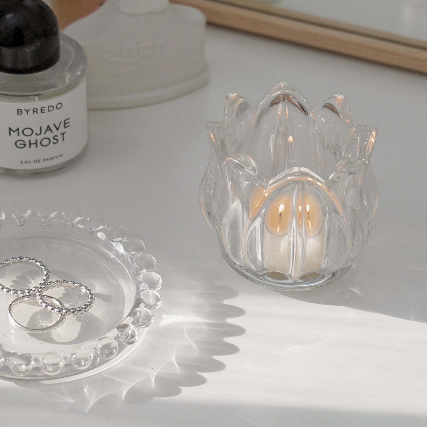 mini beaded clear round tray with silver rings and a lit tealight candle in a tulip flower shape glass tealight candle holders on vanity table with byredo, creed, and tom ford perfumes