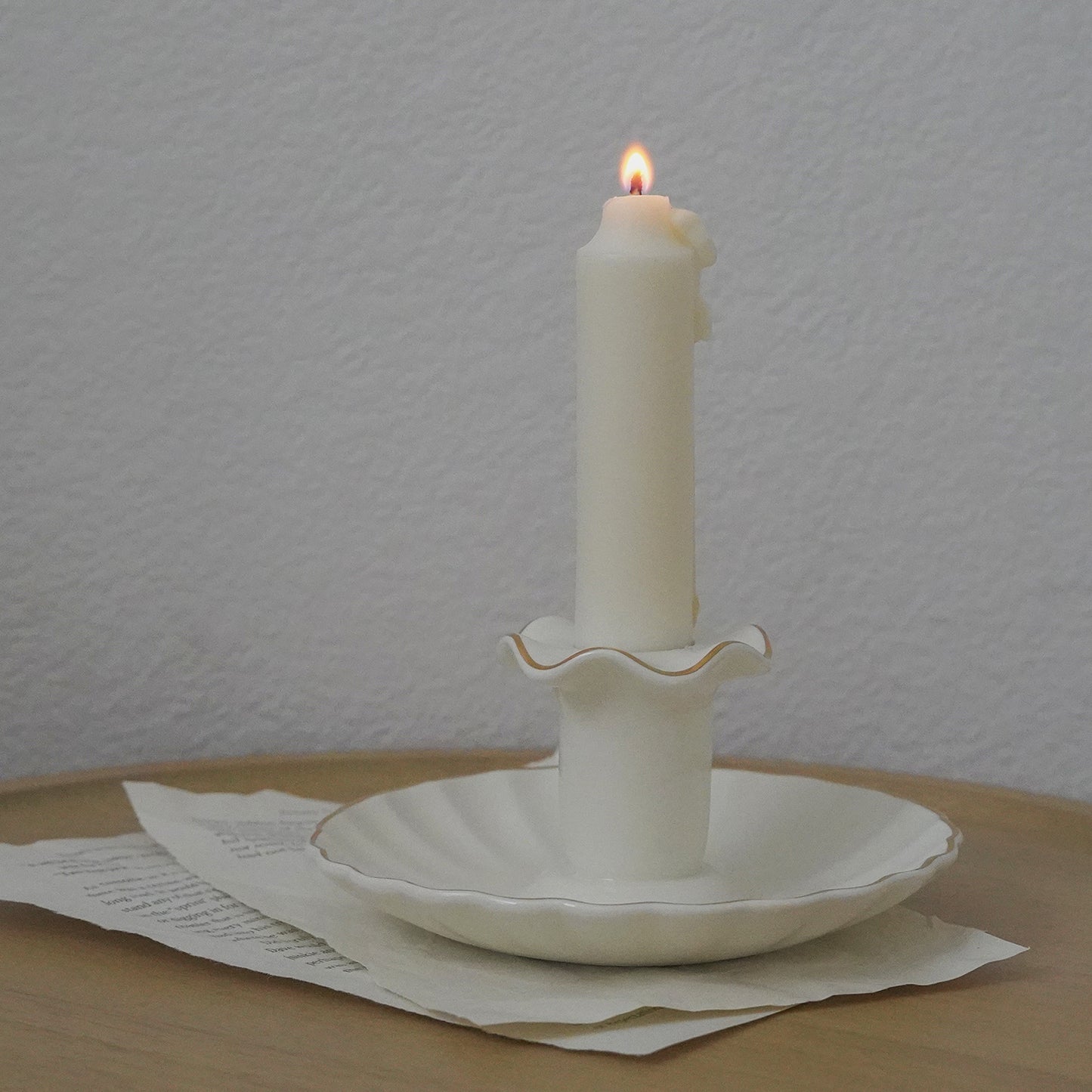 a lit white taper soy pillar candle in a white gold rim ruffle vintage candle holder on book pages