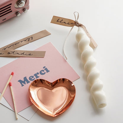 wavy spiral white soy pillar candle with beige bluewine studio ribbon, heart shape rose gold tray, merci pink postcard, matches, and pink speaker