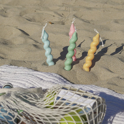 aqua blue, sage green, blush pink, tangerine yellow wavy spiral soy pillar candle in the sand, eco friendly cotton bag on picnic blanket