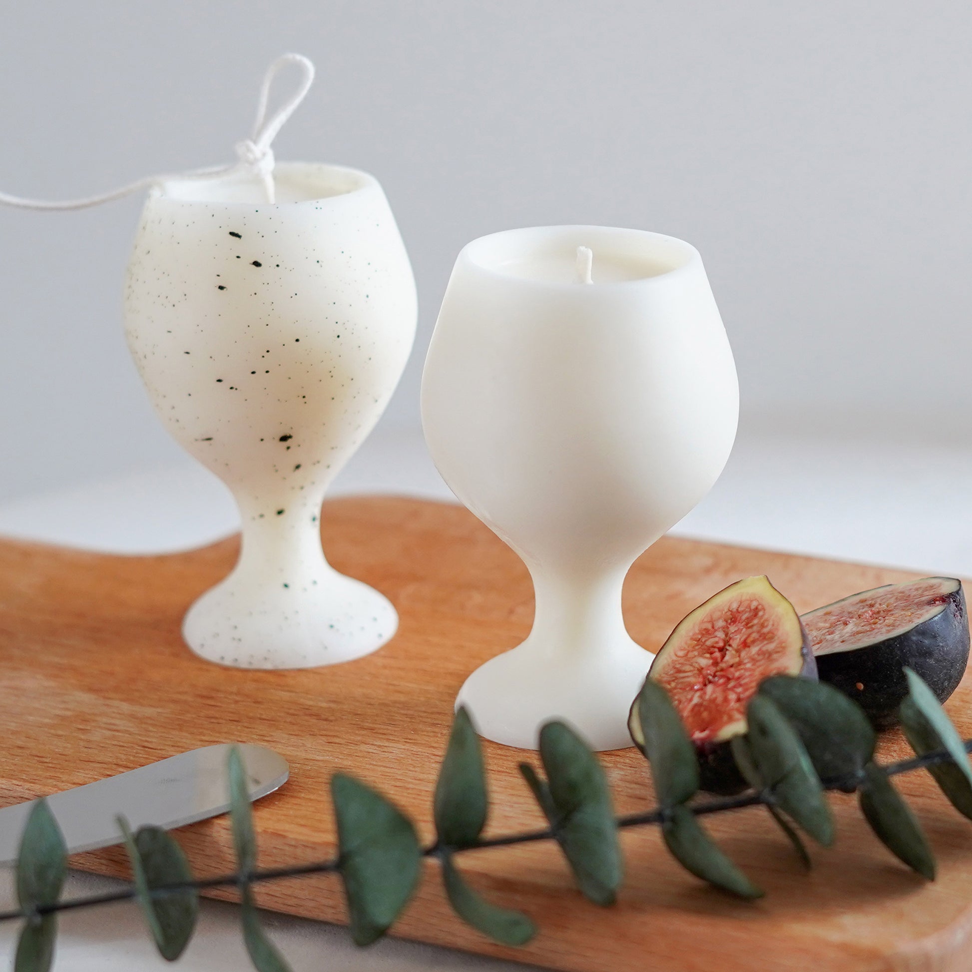 fig slices, eucalyptus leaves, cheese knife, and a dotted pattern white soy pillar wine candle, and white wine candle on ikea mini wood board