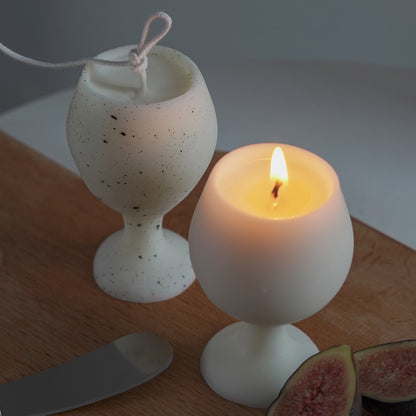 fig slices, eucalyptus leaves, cheese knife, and a dotted pattern white soy pillar wine candle, and a lit white wine candle on ikea mini wood board