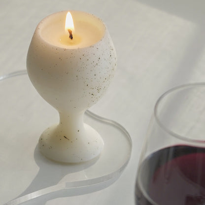 a dotted pattern white soy pillar wine candle burning on an irregular clear acrylic coaster with a glass of red wine