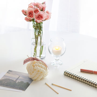 a yarn ball shape white soy pillar candle with pink bluewine studio ribbon, rolled book pages, a note, a pink pen, pink roses in a clear vase, a note, a pink pen, matches, eiffel tower postcards, pink roses in a clear vase, and a lit tealight candle in a mini glass