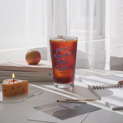 iced coffee in a 16 oz you smell like love glass, a lit cheese candle on a clear irregular shaped acrylic coaster, planner, apple, and books on the table